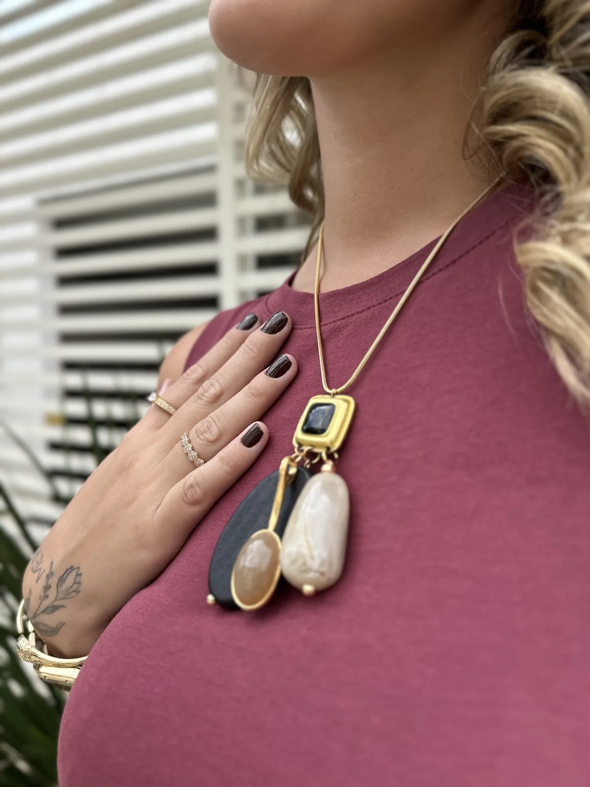 Colar longo com pendente de resina e metal dourado sobre um vestido bordô