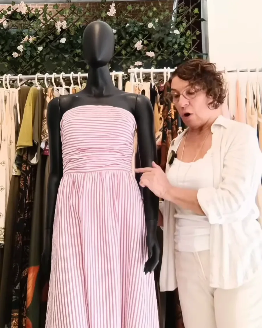 A Cláudia ajeitando um vestido listrado rosa e branco em um manequim preto