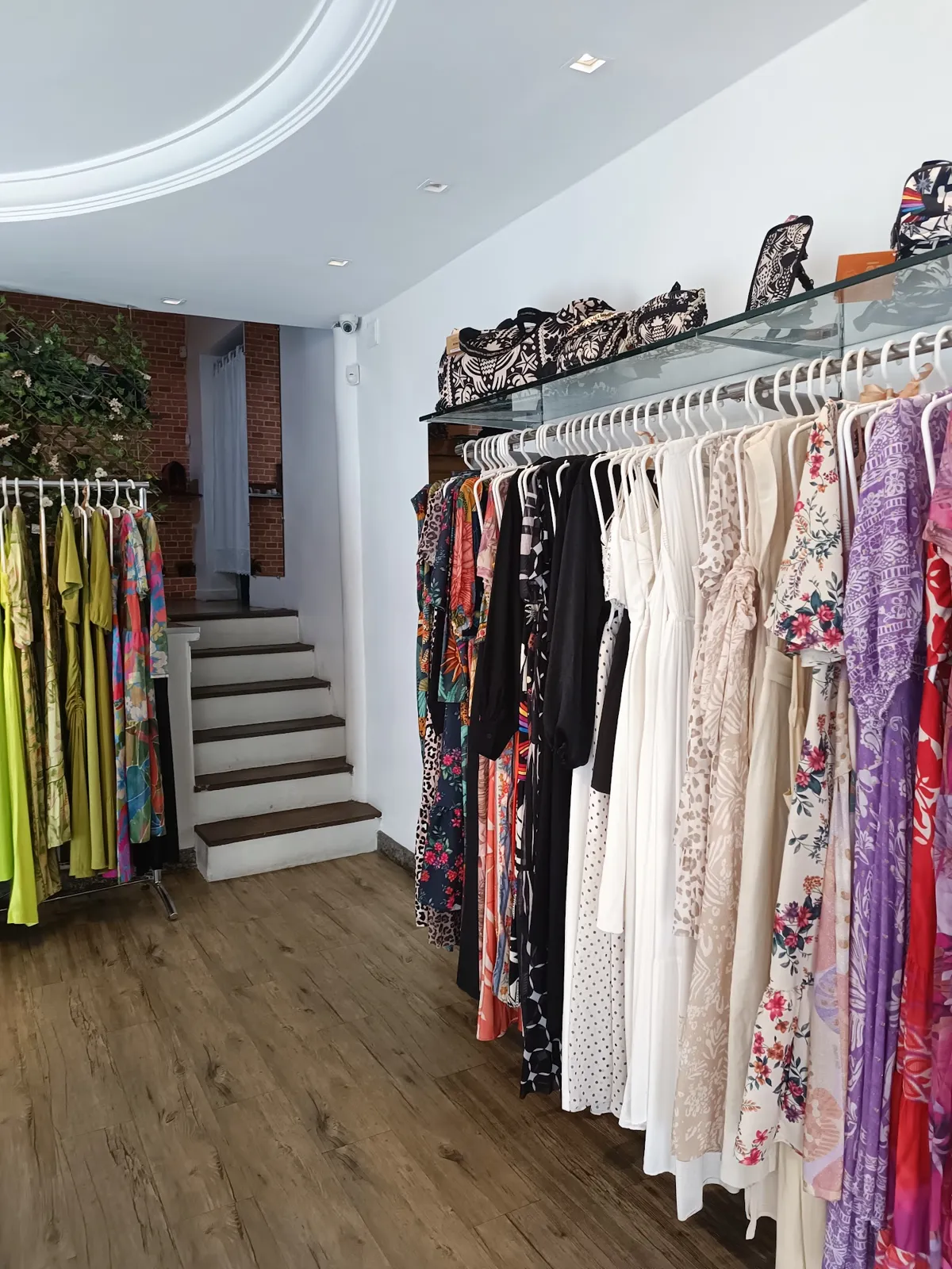 Araras da loja Virtut, com vestidos e blusas, e a escada ao fundo